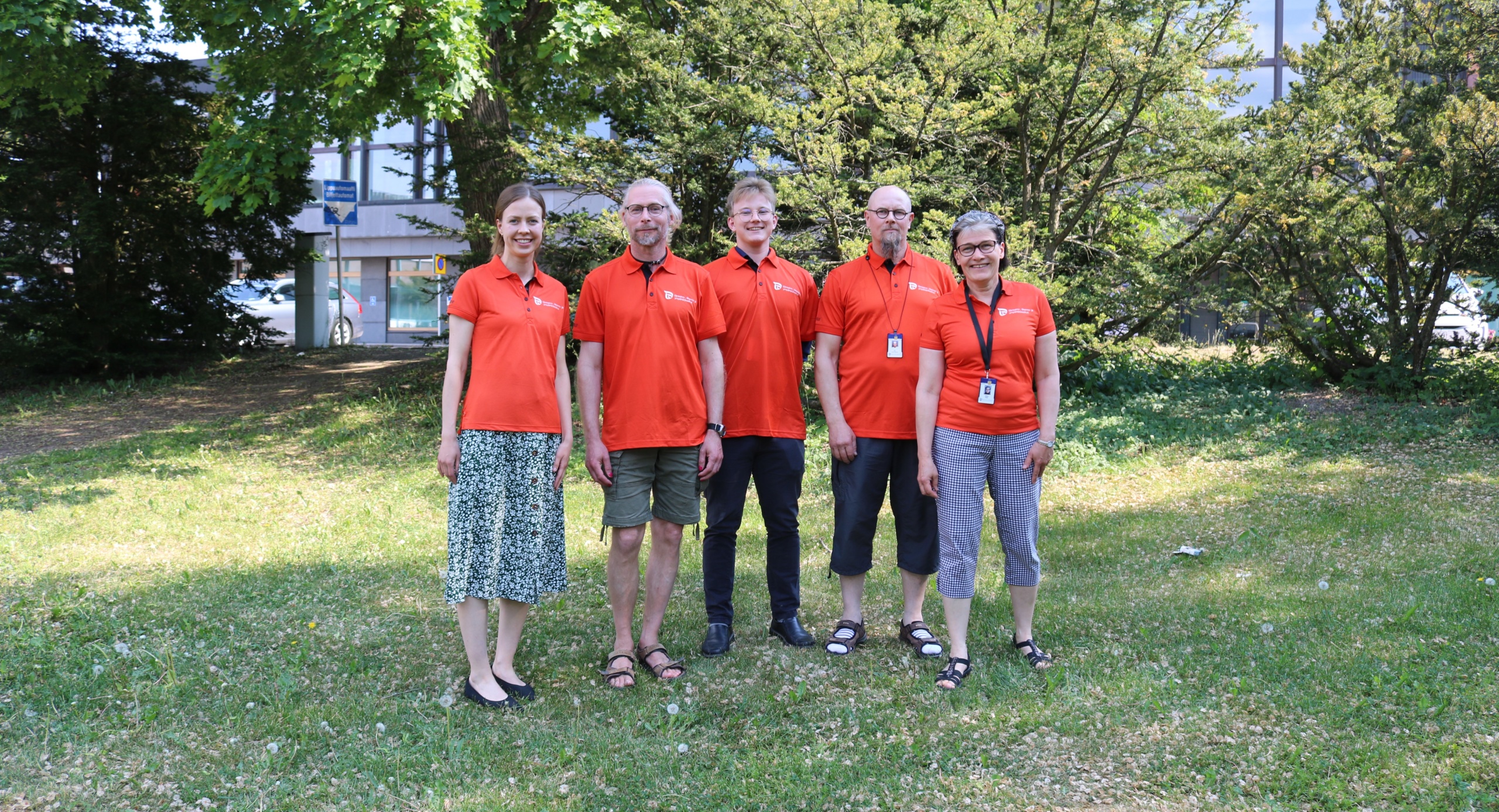 Ryhmäkuva viidestä ihmisestä oransseissa paidoissa Varsinais-Suomen ELY-keskuksen edessä.